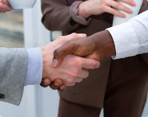 Two individuals in business attire shake hands,